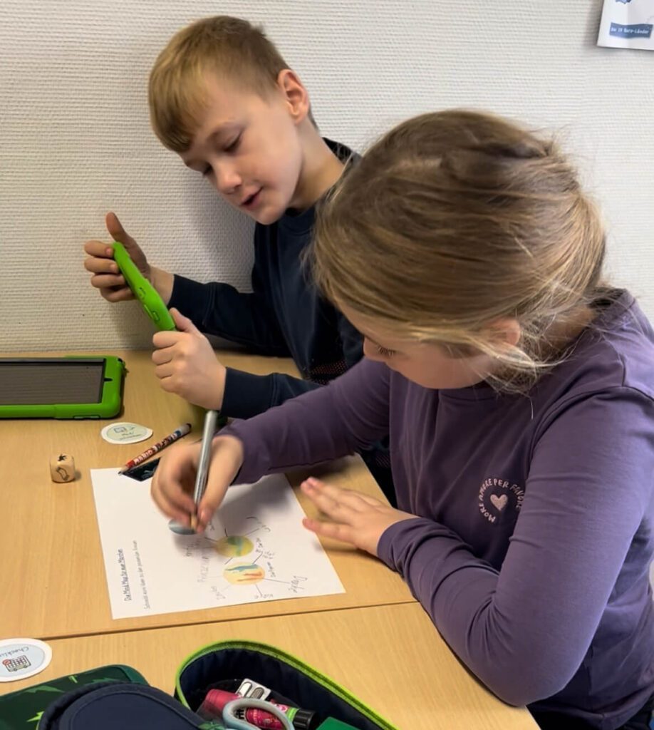 Ein Jungen und ein Mädchen sitzen an einem Tisch und erarbeiten mit einem iPad und einer Mind Map ihr Märchen.