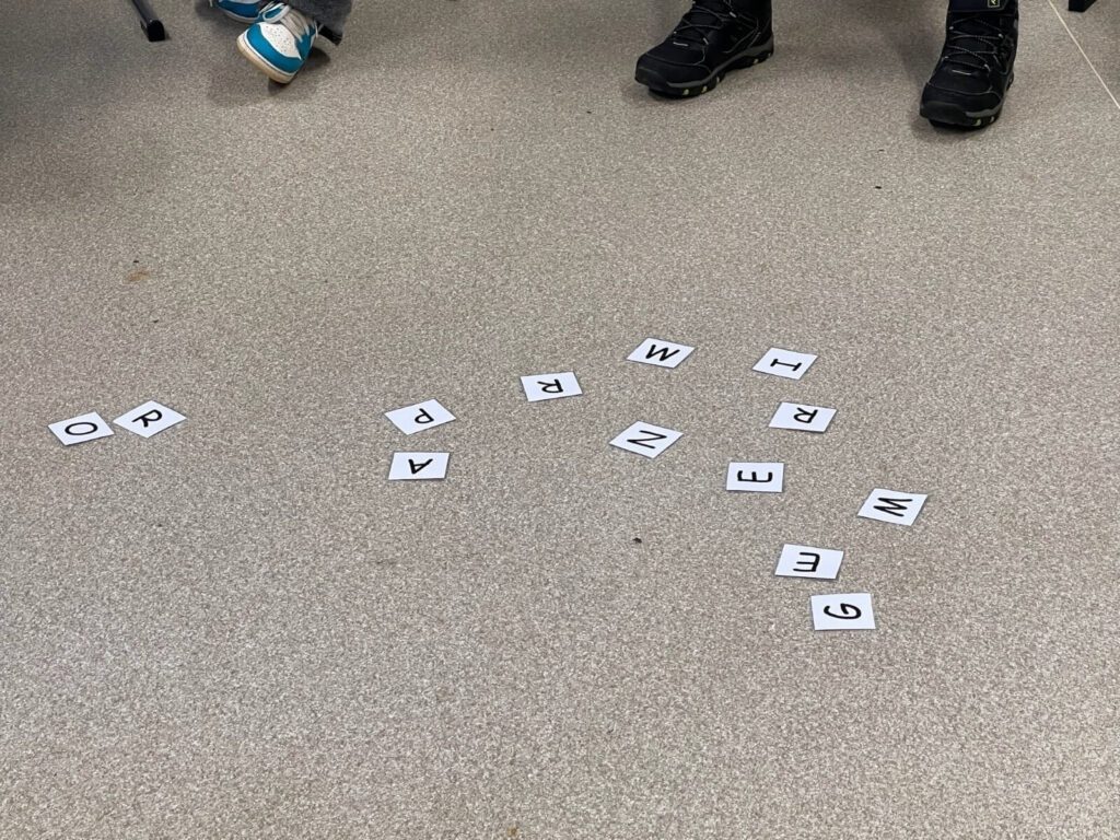 Auf dem Boden liegen Buchstaben-Schnipsel verteilt, die das Wort PROGRAMMIEREN ergeben.