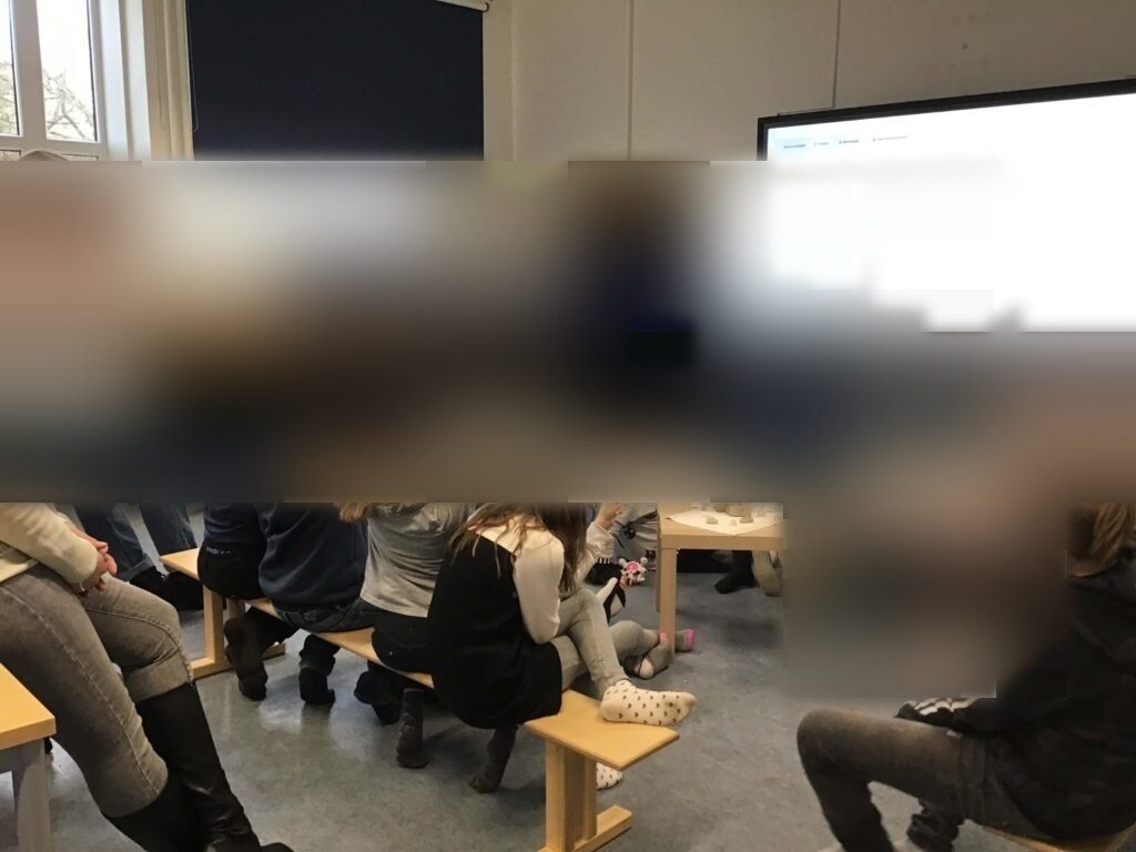 Auf dem letzten Bild ist ein Abschlusskreis zu sehen. Die Lernbegleitungen stehen vorne an der Tafel und führen die Reflexion zum Projekttag durch. Die Schüler:innen sitzen auf Bänken und melden sich. Auf dem Smartboard in der Mitte des Raumes sind die Ergebnisse der Umfrage für die Kinder geöffnet.