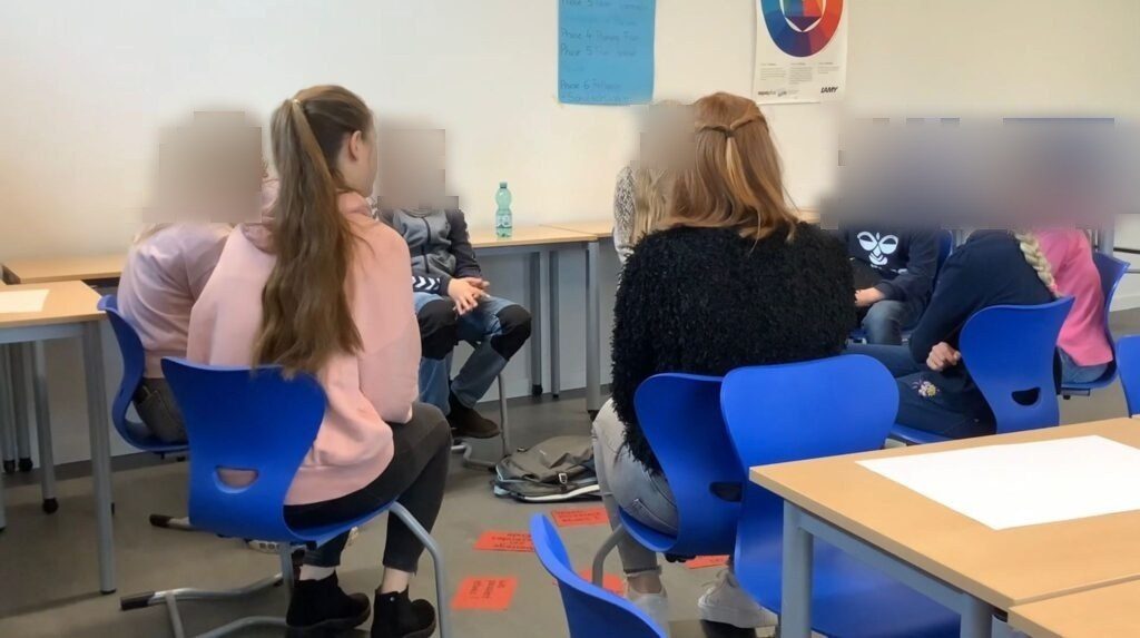 Kinder sitzen im Stuhlkreis mit den STudierenden und sprechen