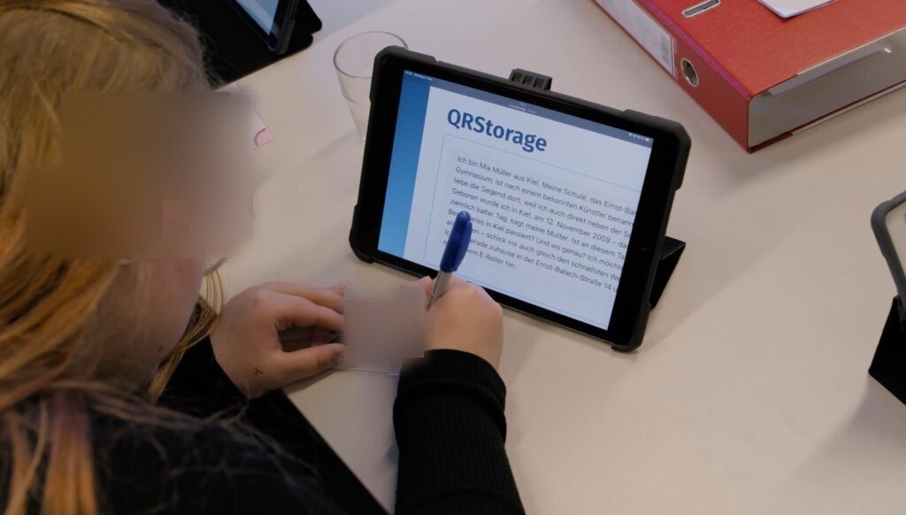 Auf einem iPad ist die geöffnete Nachricht eines Jugendlichen zu sehen. Eine Schülern trägt die persönlichen Daten aus der Nachricht auf einen Ausweis.