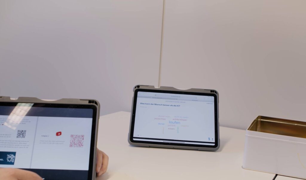 Zwei iPads stehen auf dem Tisch: Ein iPads zeigt den Book Creator mit den Aufgabenstellungen und eins die Ergebnisse in der digitalen Tafel.