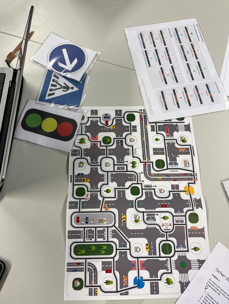 Hie sind die verwendeten Arbeitsmaterialien zu sehen, welche ausgedruckt wurden, beispielsweise ein Straßenplan, Farbcodes und Verkehrsschilder.