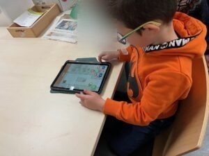 Auf dem Bild hat ein Schüler ein iPad in der Hand und übt dort mit der Beebot-App das Programmieren.