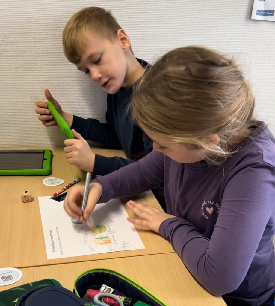 Ein Jungen und ein Mädchen sitzen an einem Tisch und erarbeiten mit einem iPad und einer Mind Map ihr Märchen.