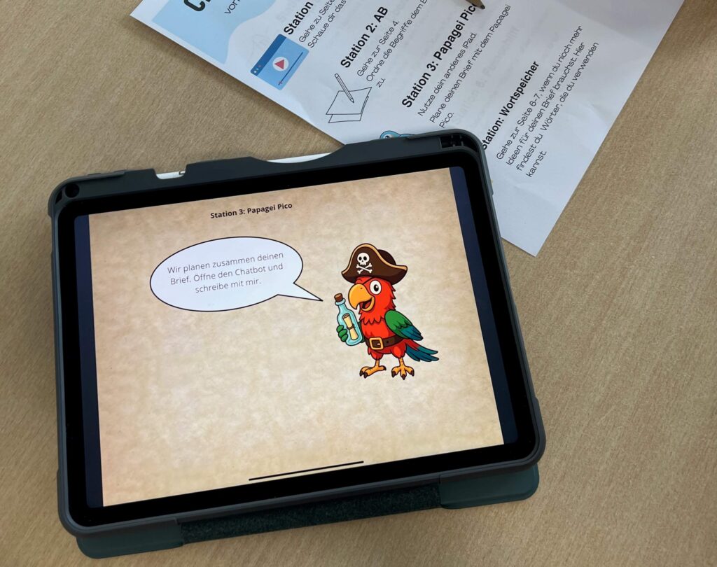 Das Foto zeigt eine Lernstation in einem Klassenzimmer oder einer ähnlichen Lernumgebung. Im Zentrum liegt ein Tablet in einer dunklen Schutzhülle auf einem hellen Holztisch. Auf dem Bildschirm des Tablets ist eine digitale Lernanwendung zu sehen, die als „Station 3: Papagei Pico“ betitelt ist.  Die Grafik auf dem Display zeigt einen bunten, illustrierten Papagei im Piraten-Look, der eine braune Kapitänsmütze mit Totenkopf-Symbol trägt und eine Flaschenpost in der Kralle hält. In einer Sprechblase steht der Text: „Wir planen zusammen deinen Brief. Öffne den Chatbot und schreibe mit mir.“ Der Hintergrund der App ist in einer hellen, pergamentartigen Optik gehalten.  Im oberen Bildrand, leicht außerhalb des Fokus, liegt ein ausgedrucktes Arbeitsblatt, das zusätzliche Instruktionen zur Station 3 enthält und Stichpunkte wie „Wortspeicher“ sowie Hinweise zur Nutzung des Chatbots aufführt. Das Bild verdeutlicht den Einsatz von Tablets und KI-gestützten Chatbots im modernen, projektorientierten Unterricht.